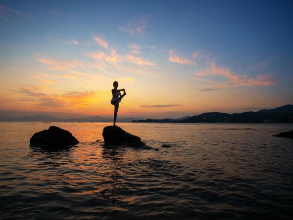 Silhouette of a person in a powerful yoga pose against a sunrise.